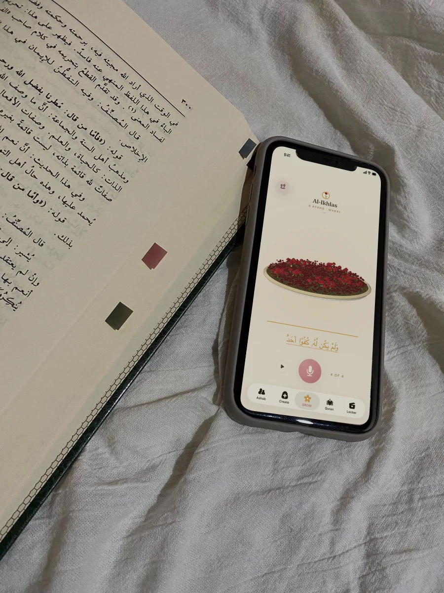 A phone displaying Hablobi beside an open Quran on linen.